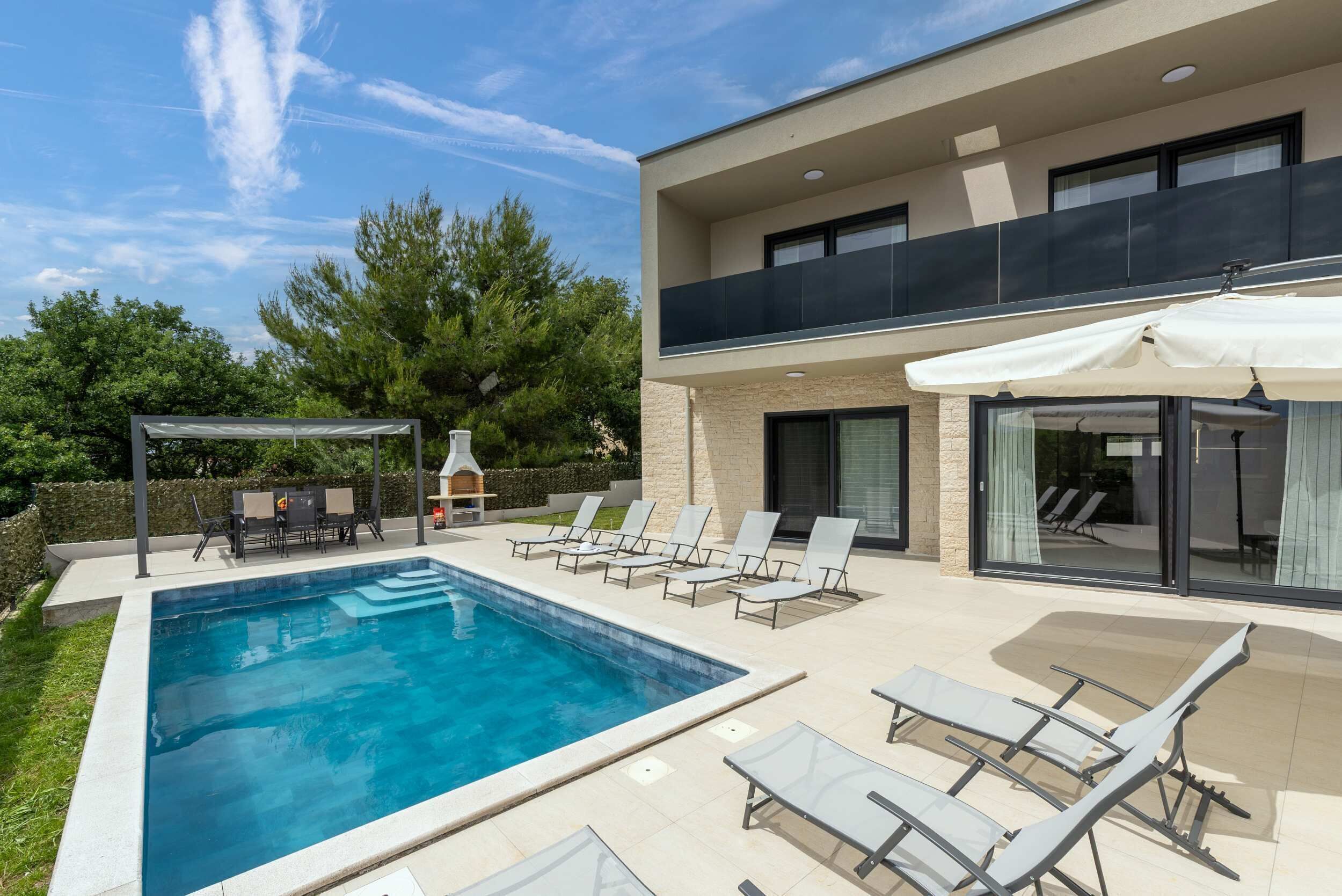 Ein modernes, zweistöckiges Haus mit Swimmingpool, Außenbereich mit Sitzgelegenheiten und einer überdachten Terrasse.