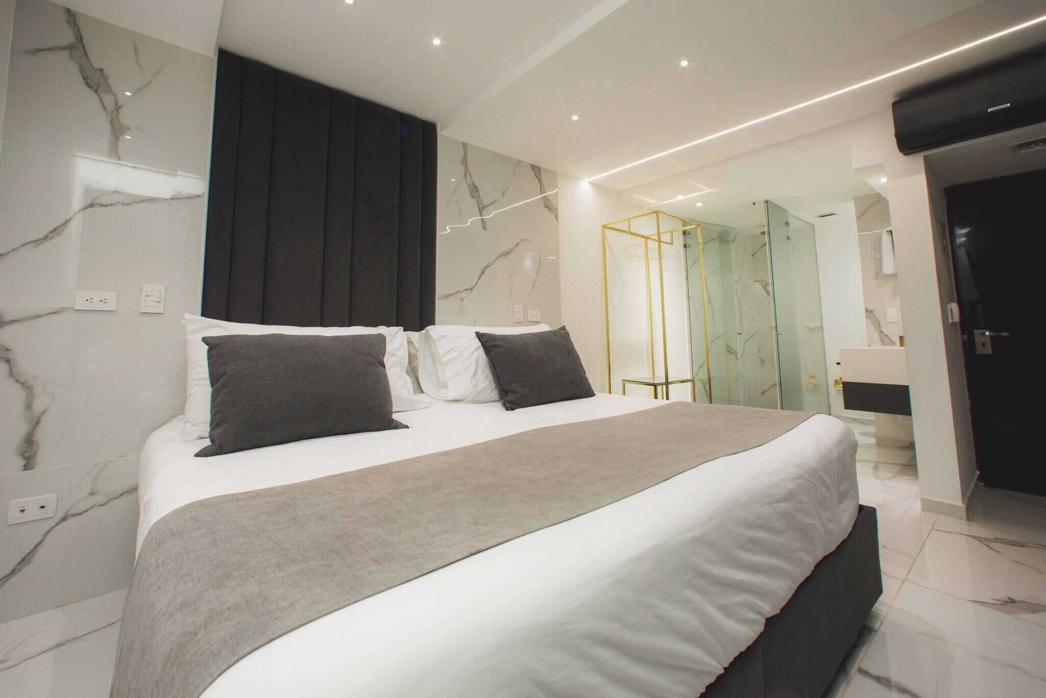 A modern bedroom with a large bed, marble walls, and a glass-enclosed shower area.
