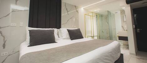 A modern bedroom with a large bed, marble walls, and a glass-enclosed shower area.