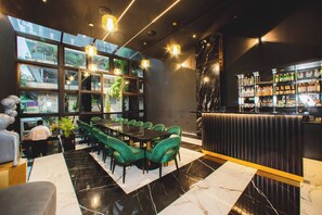 A modern bar area with a marble floor, green upholstered seating, and a bar stocked with various bottles. - Aman Luxury 23 Bedroom 3 Pool (Medellín)