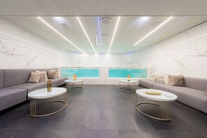 A modern lounge with a marble wall, two sofas, round tables, and a ceiling with linear lighting. - Aman Luxury 23 Bedroom 3 Pool (Medellín)