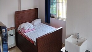 A bedroom with a wooden bed, a white sink, and a window with bars. - Village Inn Residency (Kharagpur)