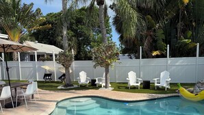 A swimming pool with a curved edge, surrounded by white chairs and a small tree. - The Pink Beach House in Delray Beach for a perfect getaway (Delray Beach)