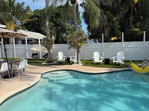 A swimming pool with a curved edge, surrounded by white chairs and a small tree. - The Pink Beach House in Delray Beach for a perfect getaway (Delray Beach)