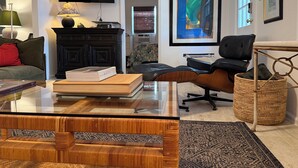 A modern living room with a glass coffee table, a black leather sofa, a black armchair, a black cabinet, and a large framed abstract painting. - The Pink Beach House in Delray Beach for a perfect getaway (Delray Beach)