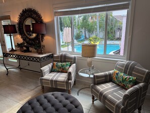 A living room with striped armchairs, a tufted ottoman, a side table, a lamp, and a large mirror. - The Pink Beach House in Delray Beach for a perfect getaway (Delray Beach)