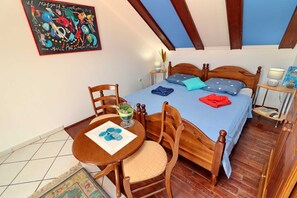 Ein Schlafzimmer mit einem Bett, einem Holzstuhl, einem kleinen Tisch, einem Gemälde und einem Fliesenboden.