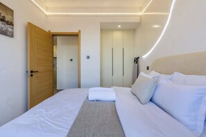 A bedroom with a bed, a wooden door, a wardrobe, and a painting on the wall. - City-view 1BR near Junction mall,Gym,pool access (Nairobi)