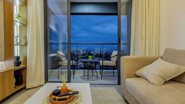 Una sala de estar con un sofá, una mesa de centro con un control remoto y un balcón con vistas a la ciudad.