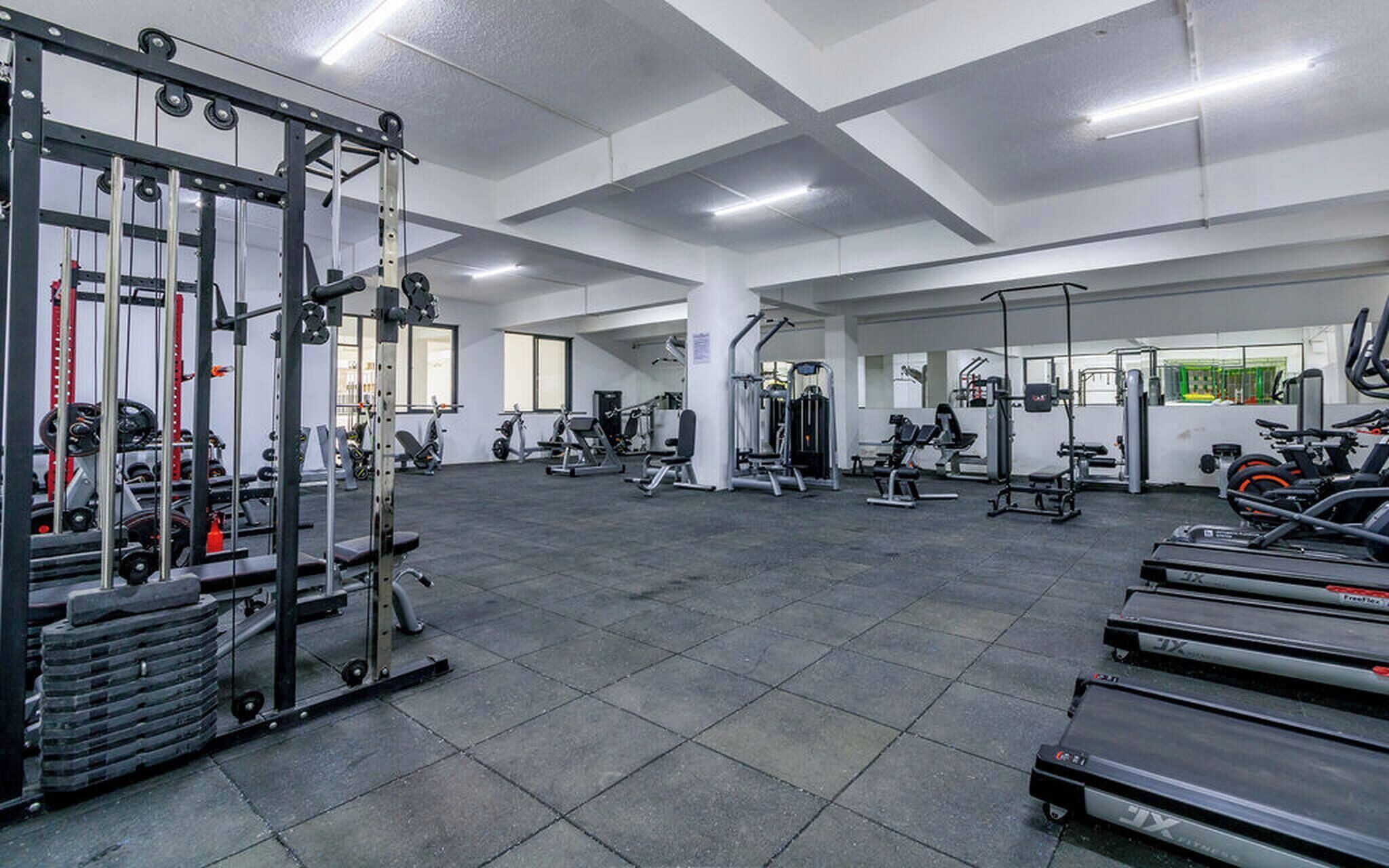 Une salle de sport équipée de divers appareils d’exercice, notamment des tapis de course, des appareils de musculation et des poids libres.