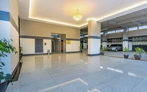 A modern building with a clean, polished floor, a central chandelier, and a parking garage in the background. - City-view 1BR near Junction mall,Gym,pool access (Nairobi)