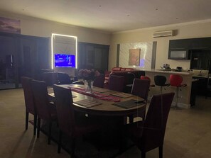 Un comedor con una mesa redonda, sillas rojas, un jarrón de flores y un televisor al fondo.