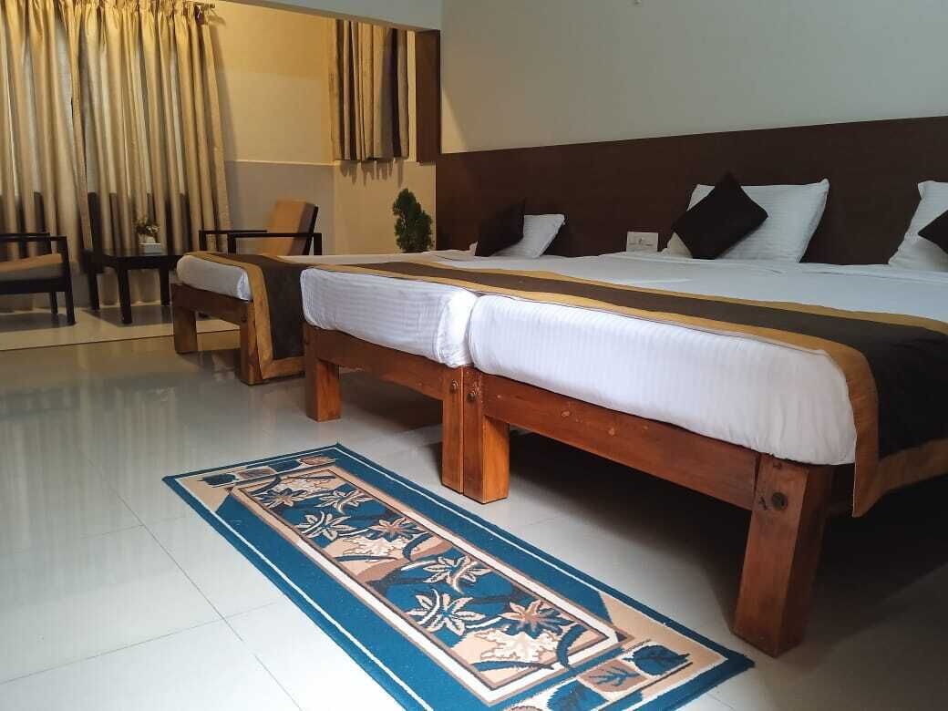A double bed with a wooden frame, a matching bench, a patterned rug, and a room with curtains and a plant.