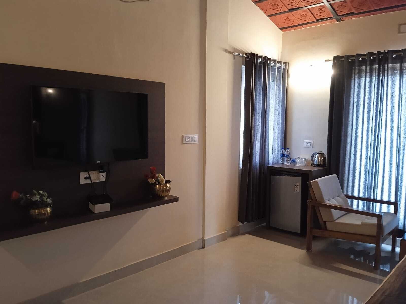 A modern living room with a flat-screen TV, a small table with a kettle, and a chair.