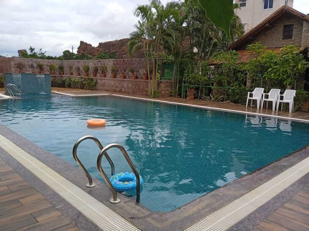 Una piscina con trampolín, sillas de descanso y un muro de piedra con plantas.