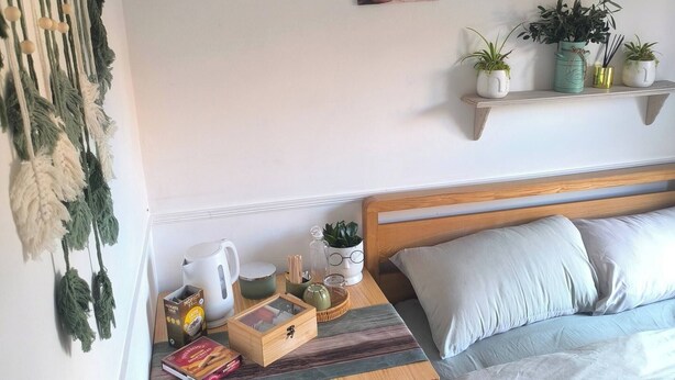 Una camera da letto con un letto, un comodino, una scrivania e una sedia. Sono presenti decorazioni a parete e uno scaffale con piante.