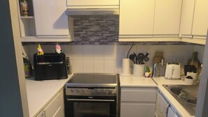 Una cucina compatta con mobili bianchi, un fornello, forno, lavastoviglie e microonde.