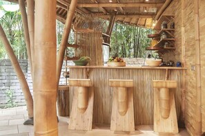 A bamboo-themed bar area with stools, shelves, and a fruit bowl. - Cacao House Eco-Luxe Family home near Green School (Kecamatan Abiansemal)