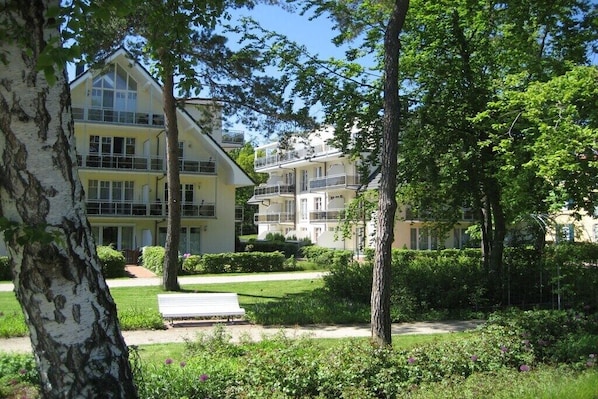 Ein mehrgeschossiges Wohngebäude mit Gartenanlage, einer Bank und einem Weg.