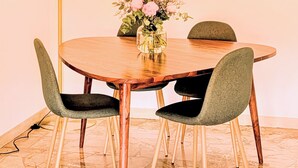 Ein runder Holztisch mit vier Stühlen, einer Blumenvase und einer Stehlampe.