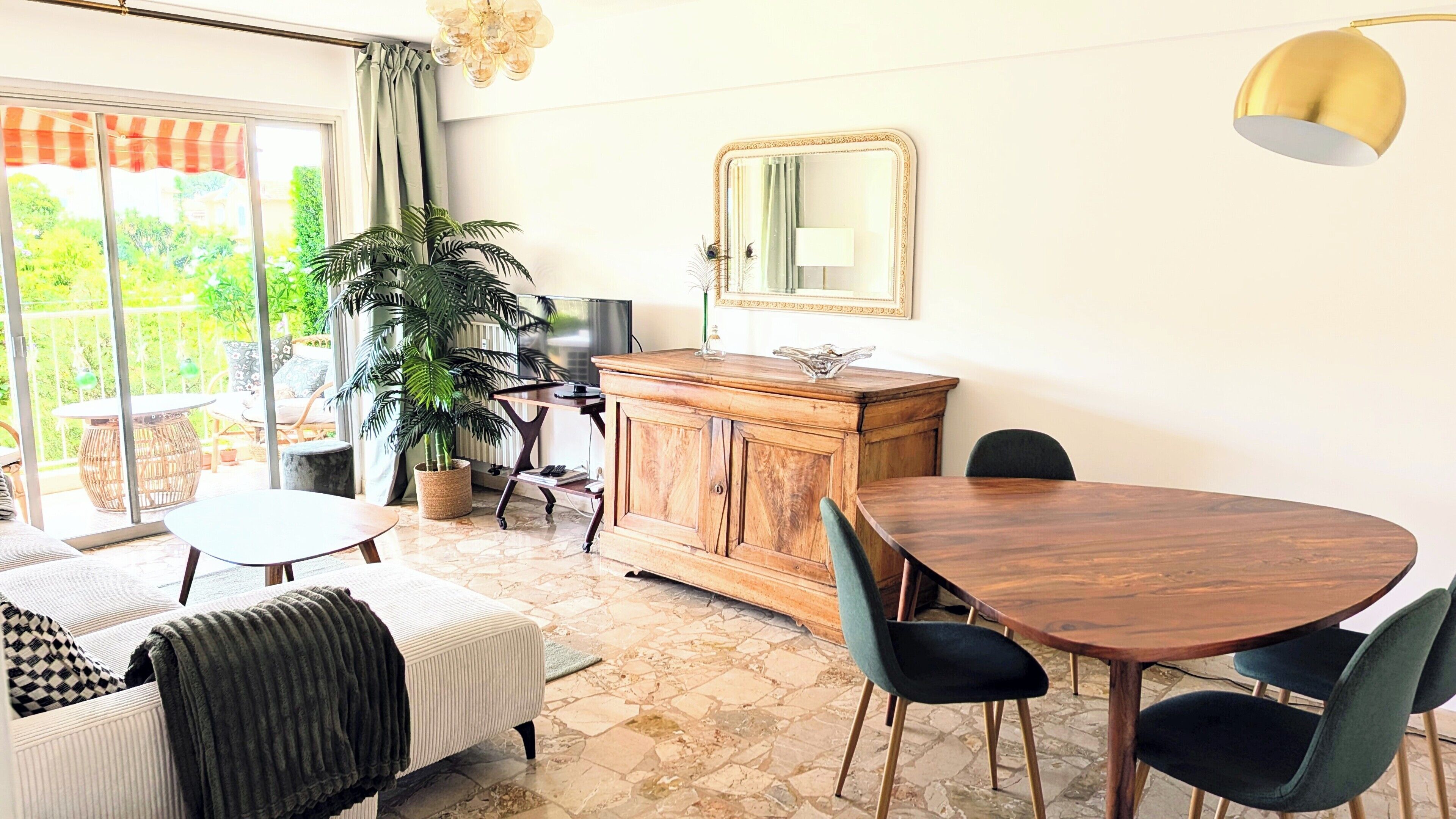 Een eetruimte met een houten tafel en stoelen, een kast, een spiegel en een grote potplant.