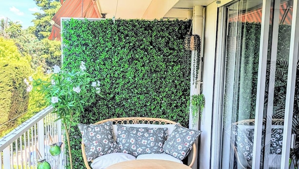Ein Balkon mit Korbmöbeln, einem runden Tisch und einer grünen Wand.