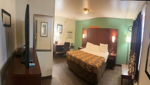 A hotel room with a bed, a desk, a television, and a chair. - King Bed|Smoking|Aurora (Aurora, IN)