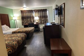 Ein Hotelzimmer mit zwei Betten, einem Schreibtisch, einem Stuhl, einer Lampe, einem Fernseher und einem Spiegel.