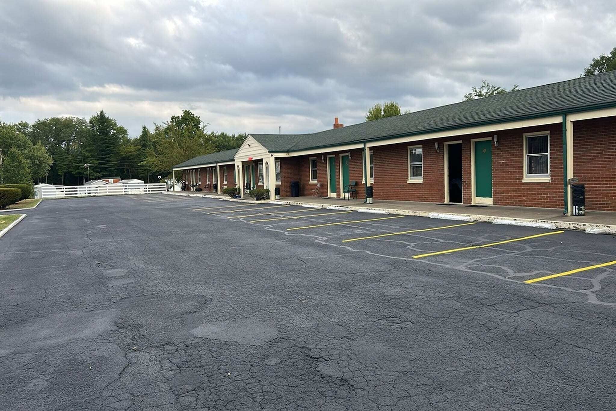 A row of motel rooms with a parking lot in front.