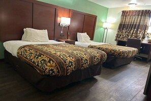 Hotellihuone, jossa on kaksi sänkyä, työpöytä, tuoli ja lamppu.