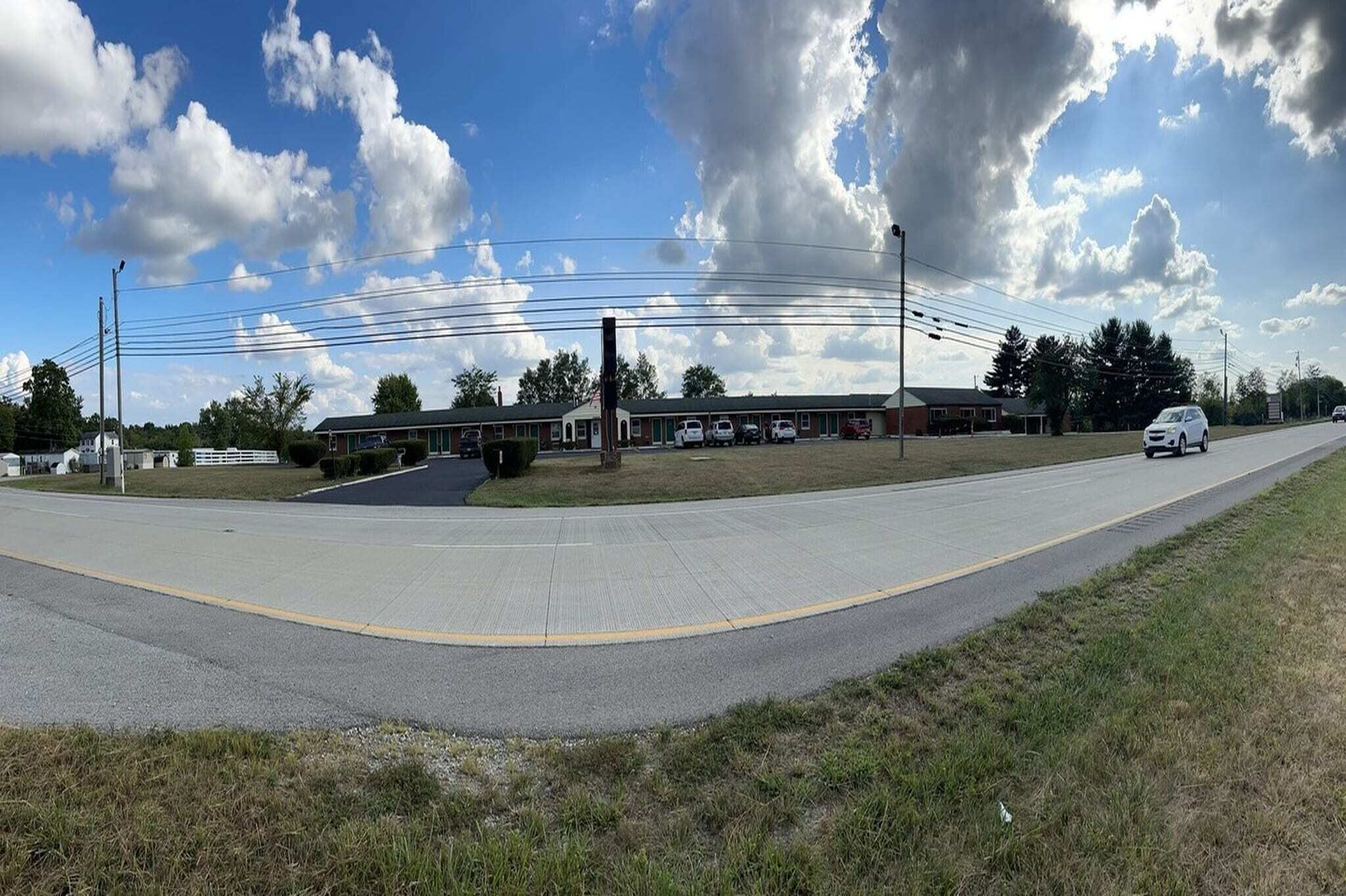 A road with a building in the background, a sidewalk, and a grassy area.