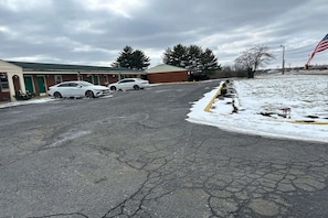 A parking lot with two white cars, a building with a green door, and a snow-covered ground.