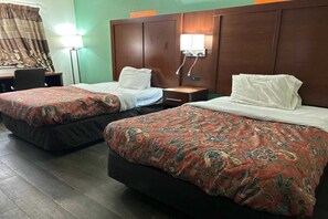 Habitación de hotel con dos camas, cada una con una colcha estampada, cabecero de madera, mesitas de noche y una lámpara.