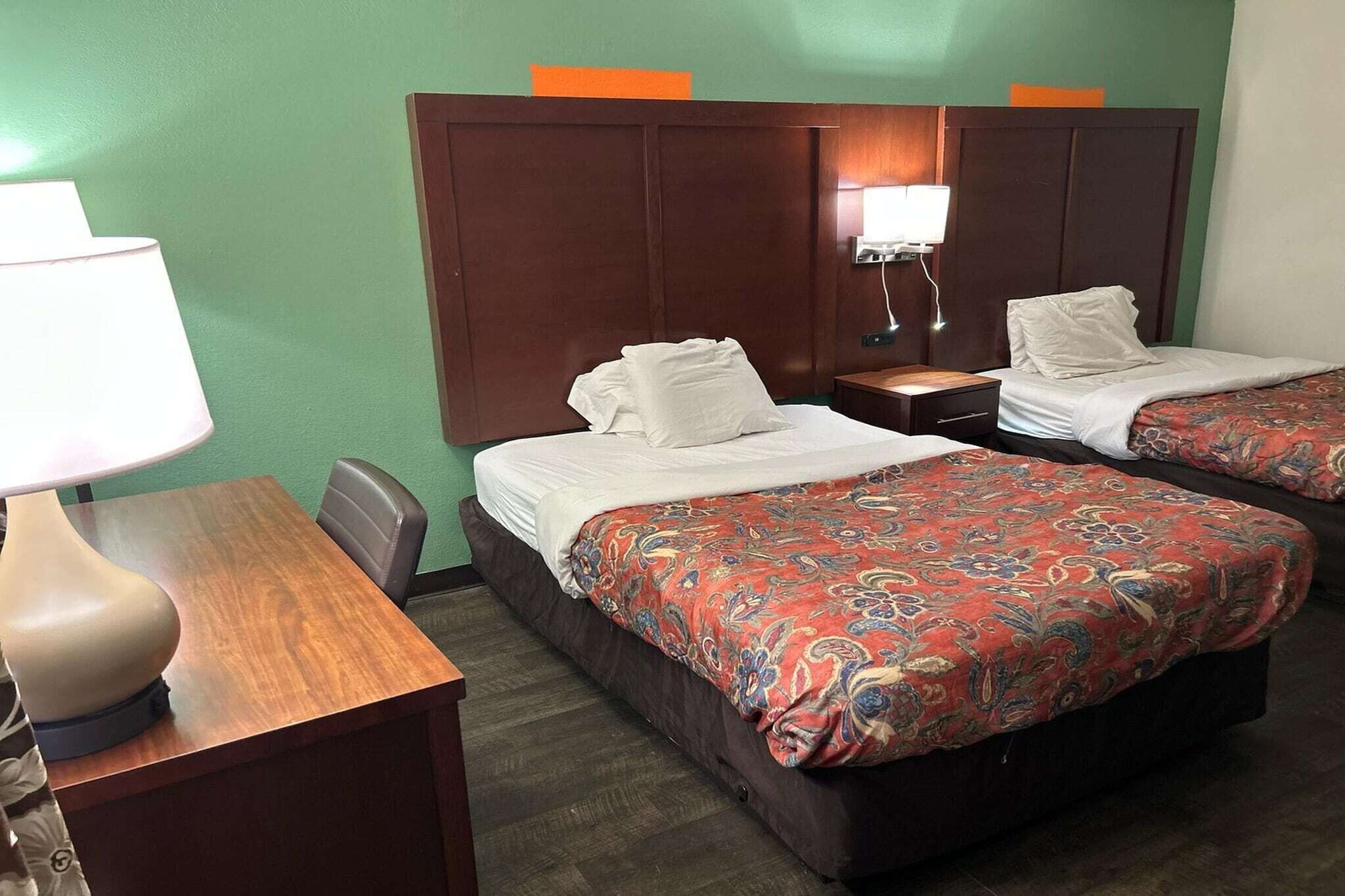 Een hotelkamer met twee bedden, een bureau met een lamp en een nachtkastje met een lamp.