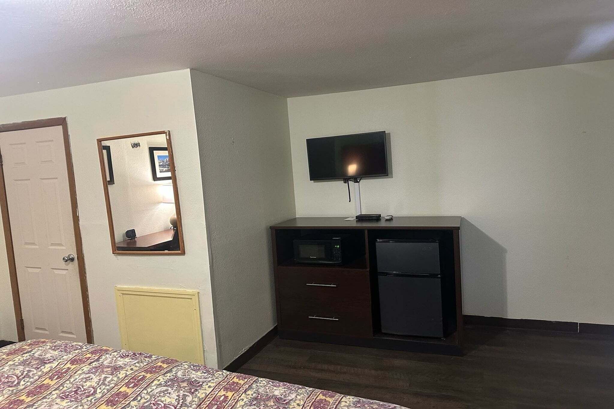 Une chambre d’hôtel comprenant un lit, une commode avec un téléviseur, un four à micro-ondes et un réfrigérateur.