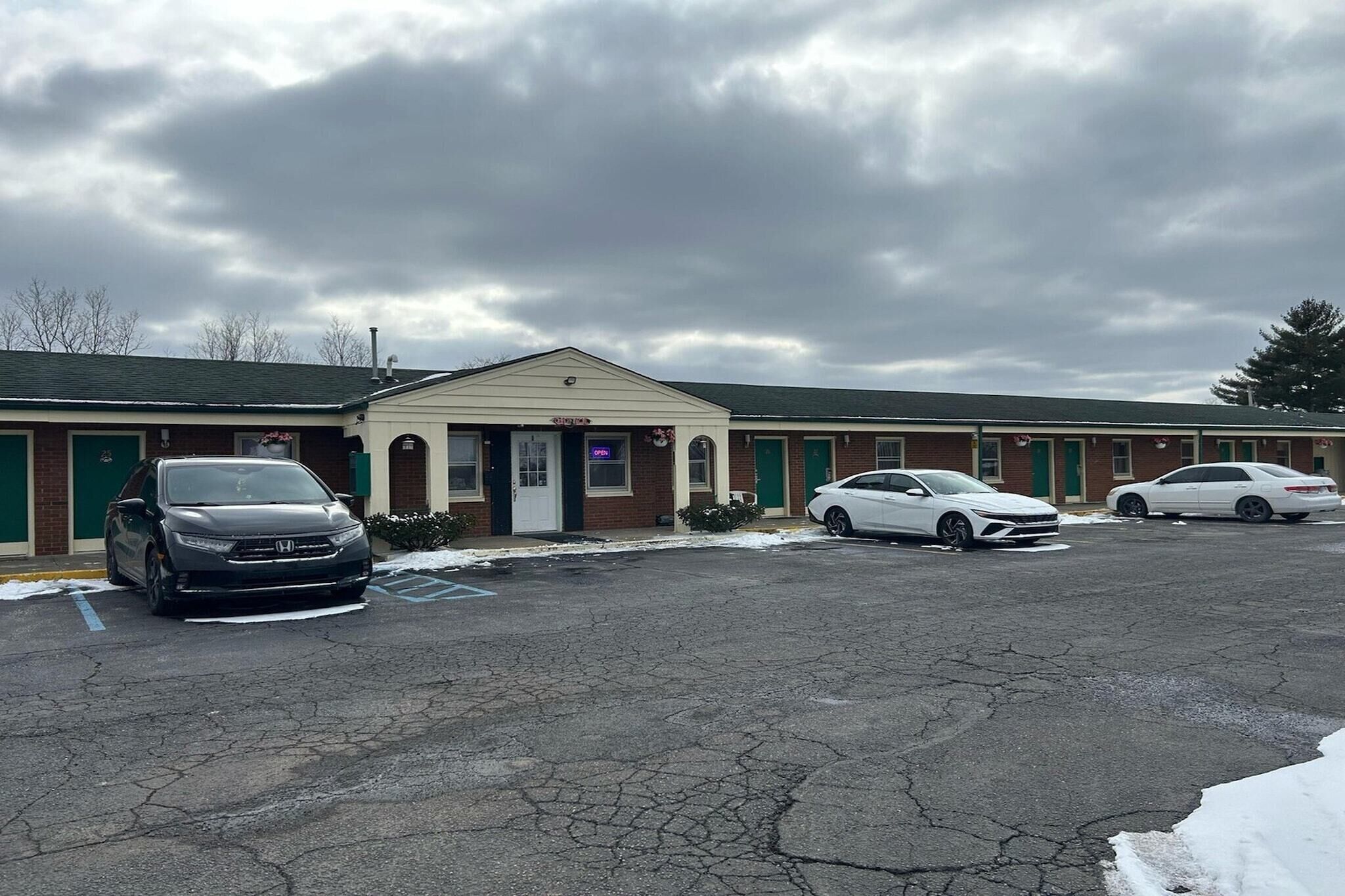 Un motel avec une entrée principale, un parking et trois voitures garées devant.