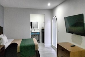 A hotel room with a bed, a desk, a mirror, a television, and a wardrobe. - Junior Room with Queen Bed|Nsmk (Barstow CA)