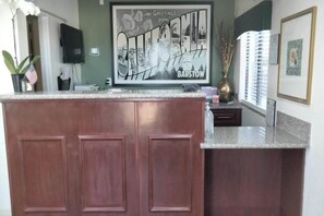 Una cocina con una isla de madera, un televisor montado en la pared y un letrero de bienvenida enmarcado.