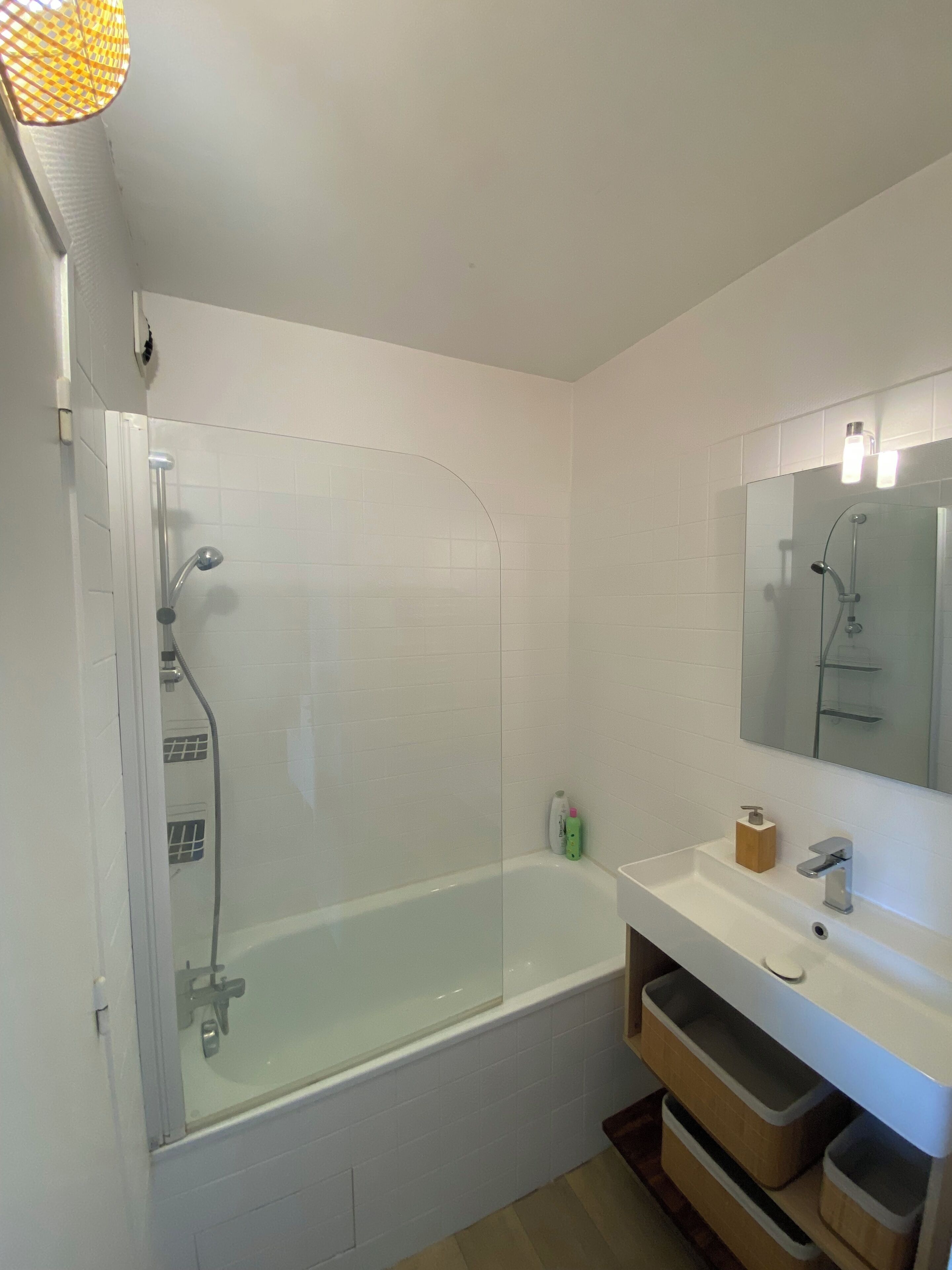 Un bany modern amb dutxa de vidre, un lavabo blanc amb mirall i calaixos de fusta per a l'emmagatzematge.