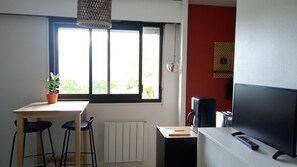 A small kitchen with a window, a table with chairs, a radiator, a TV, and a speaker. - CLEO*VALVES*PARKING (Vannes)