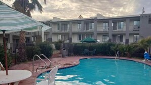 A swimming pool with a poolside area, including a table and chairs, surrounded by a fence and a building in the background.