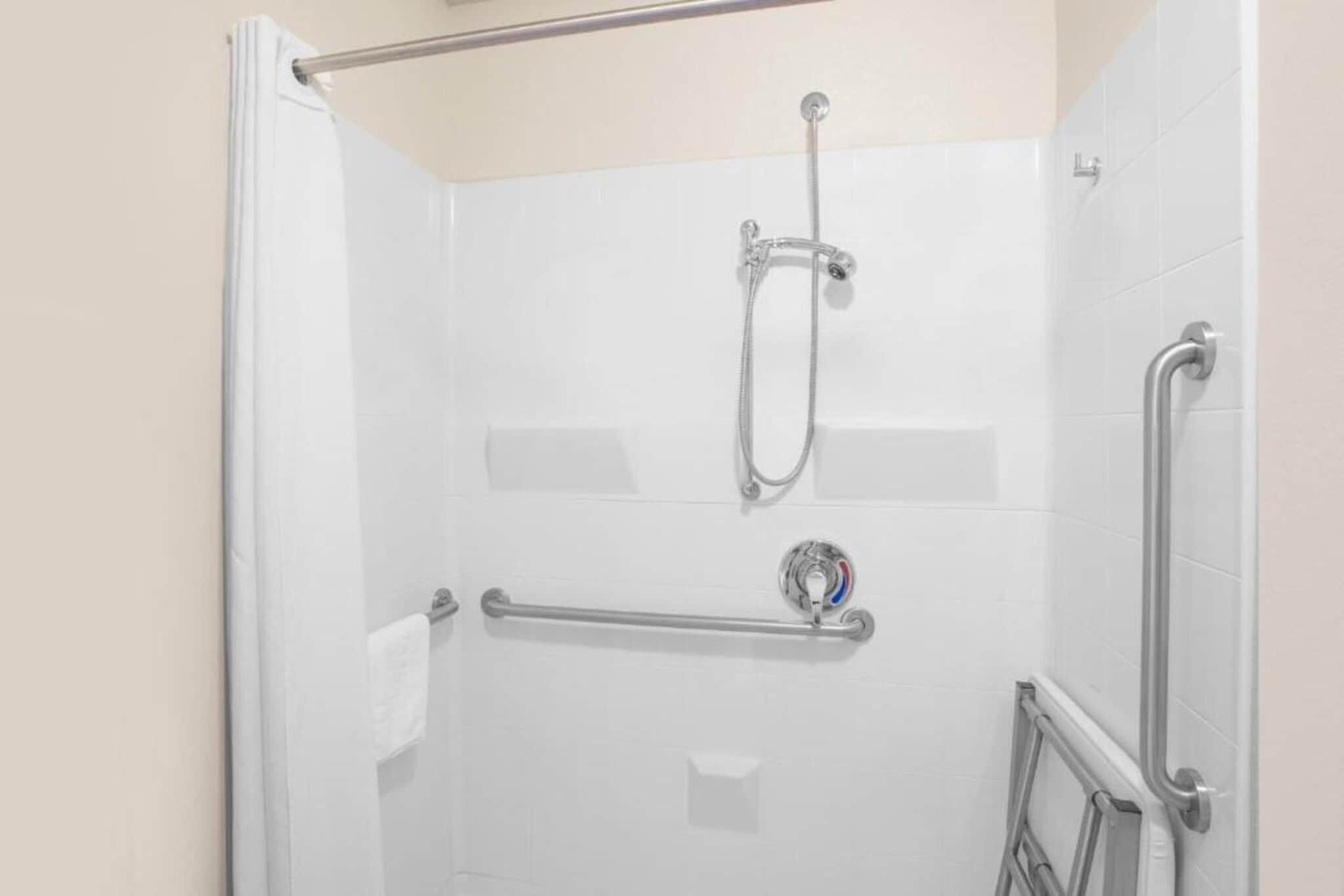 A shower with a grab bar, a handheld showerhead, and a wall-mounted faucet.