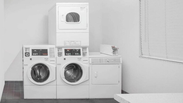 A laundry room with stacked washers and dryers, a small table with a book, and a window with blinds.