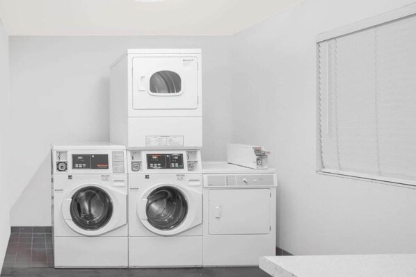 A laundry room with stacked washers and dryers, a small table with a book, and a window with blinds.