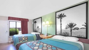 Habitación de hotel con dos camas, un escritorio con lámpara, teléfono y un cuadro grande con palmeras.