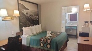 Et hotelværelse med en seng, et skrivebord, en stol, et badeværelse med et spejl og en væglampe.