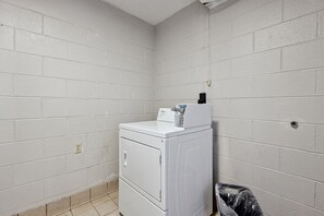 A laundry room with a stacked washer and dryer, a trash bin, and a power outlet on the wall.