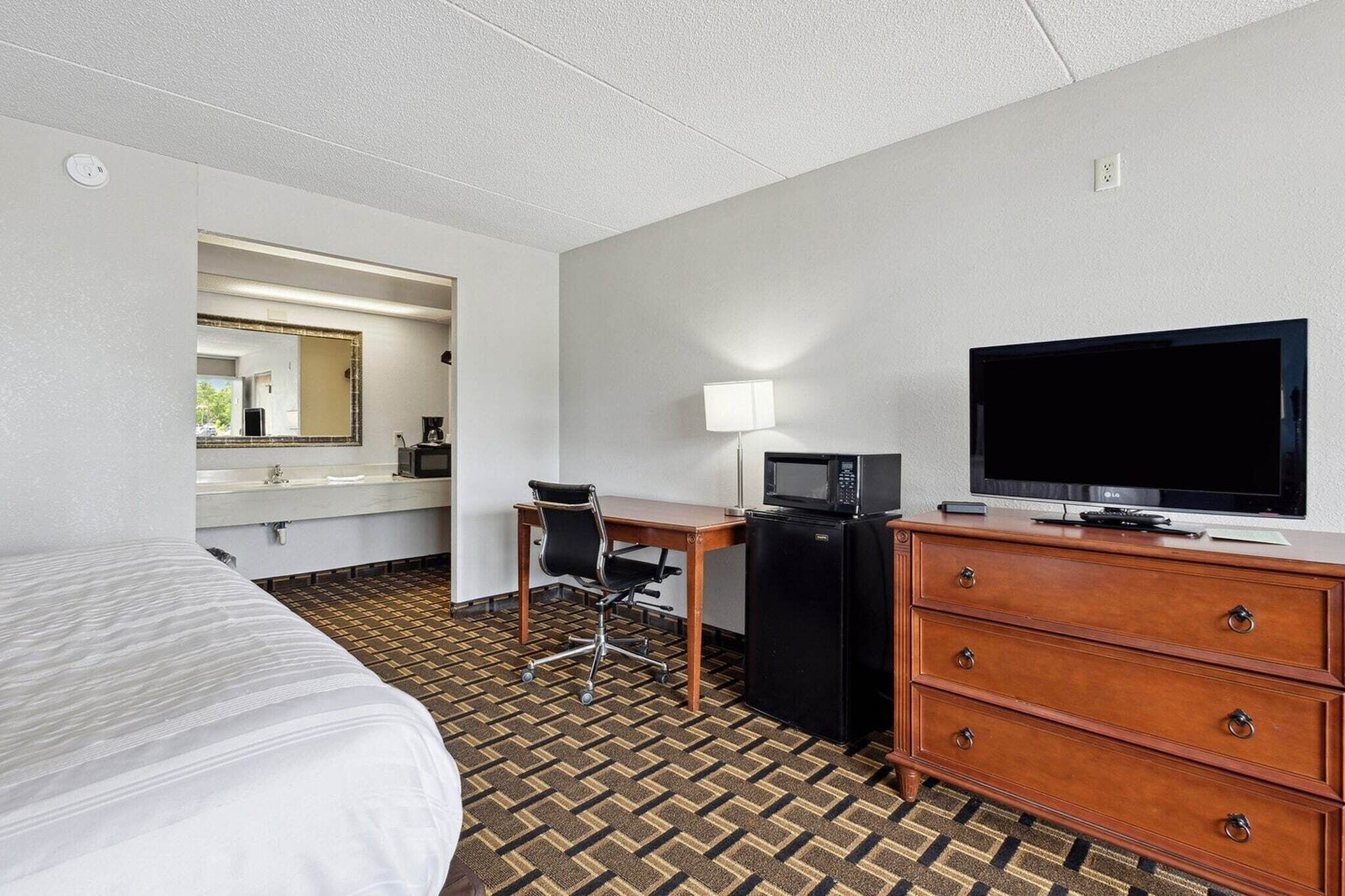 Ein Hotelzimmer mit einem Bett, einem Schreibtisch mit Stuhl, einem Fernseher, einer Mikrowelle und einem Schrank.