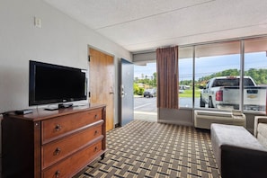 Habitación de hotel con televisor sobre una cómoda, puerta corredera de vidrio que da a un aparcamiento y vistas a vehículos estacionados.