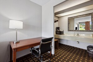 Habitación de hotel con un escritorio de madera, una silla de oficina negra, una lámpara blanca, un microondas, un lavamanos y un espejo grande.